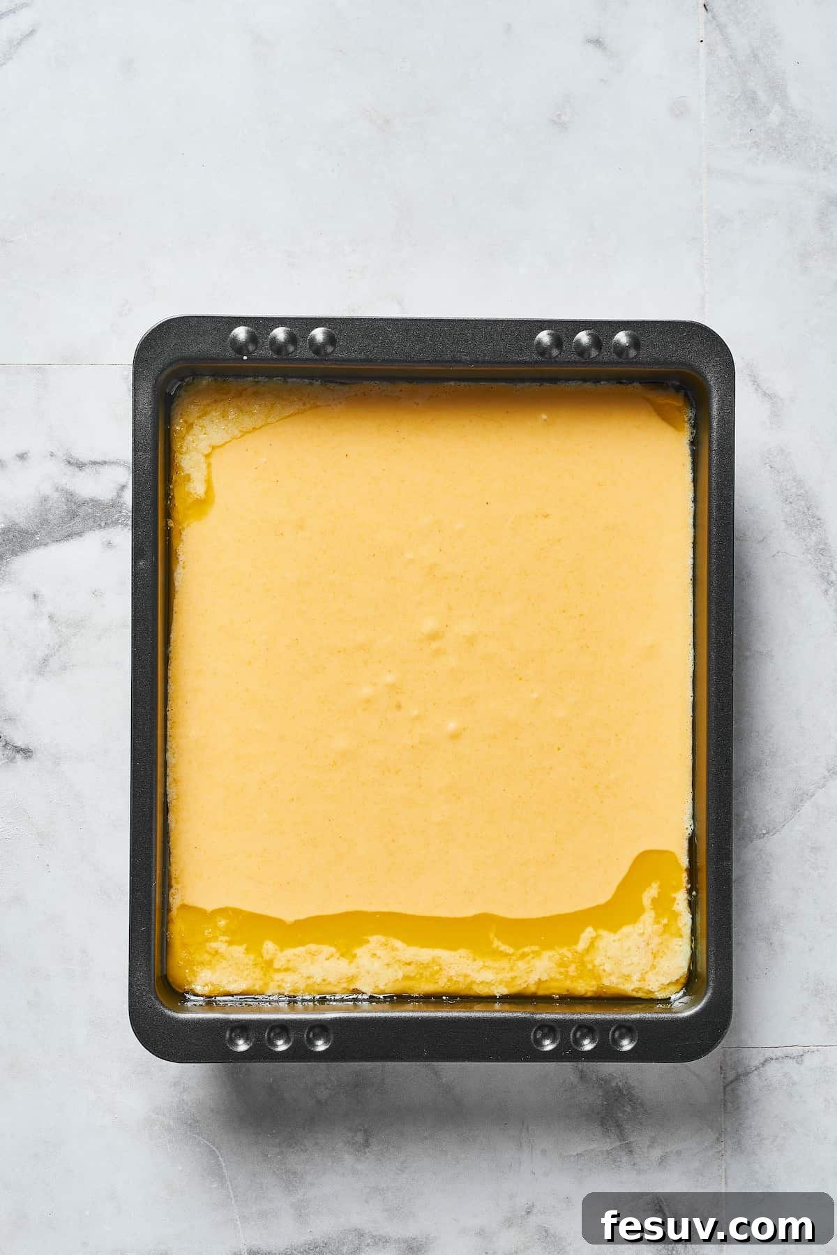 Smooth cornbread batter poured evenly into a well-greased baking pan, ready for the oven to transform it into a golden loaf.