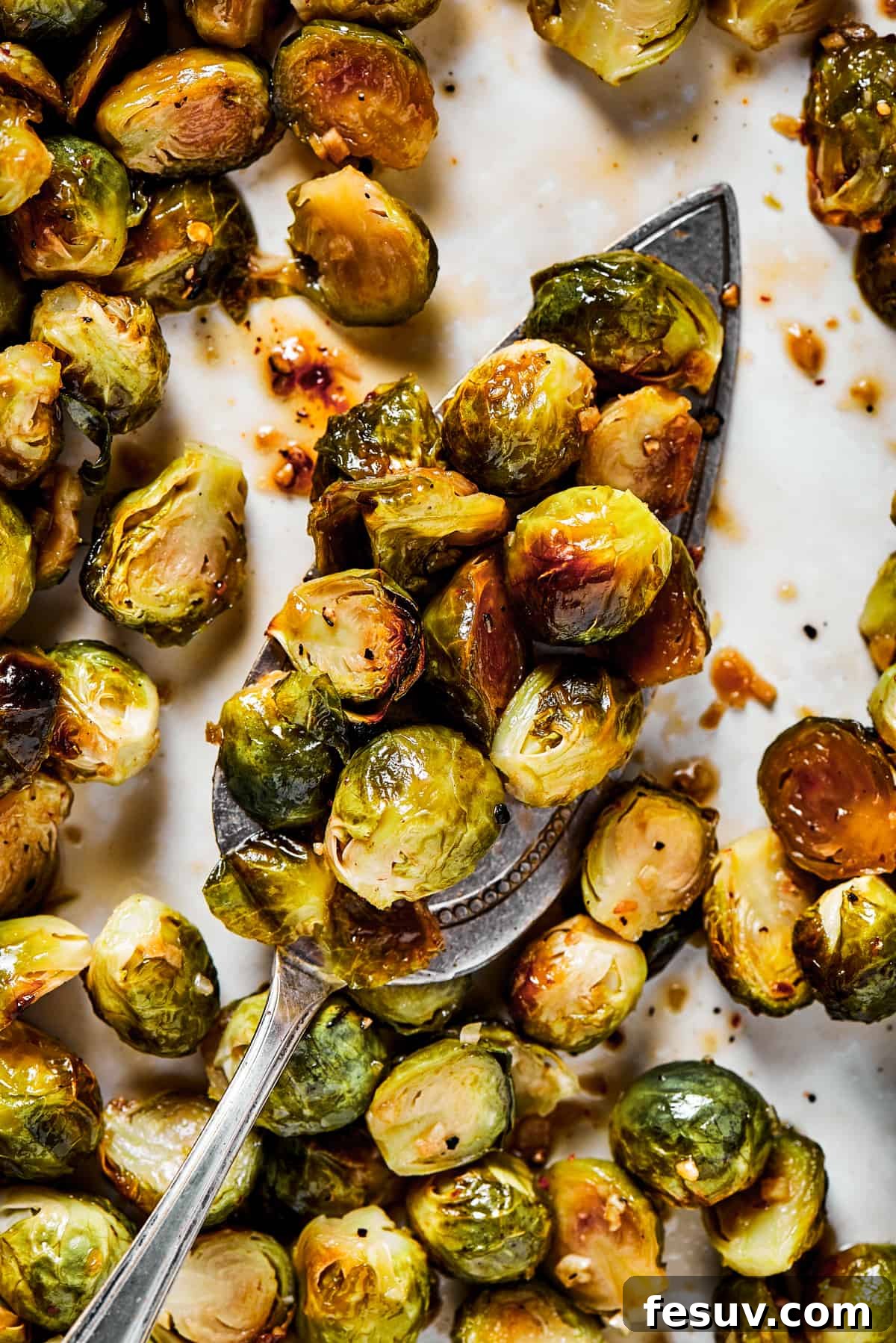 These Roasted Brussels Sprouts are oven-roasted with garlic and drizzled with a killer maple-pomegranate glaze. A veggie side you’ll crave! A tray of roasted brussel sprouts with a silver serving spoon, ready to be served.