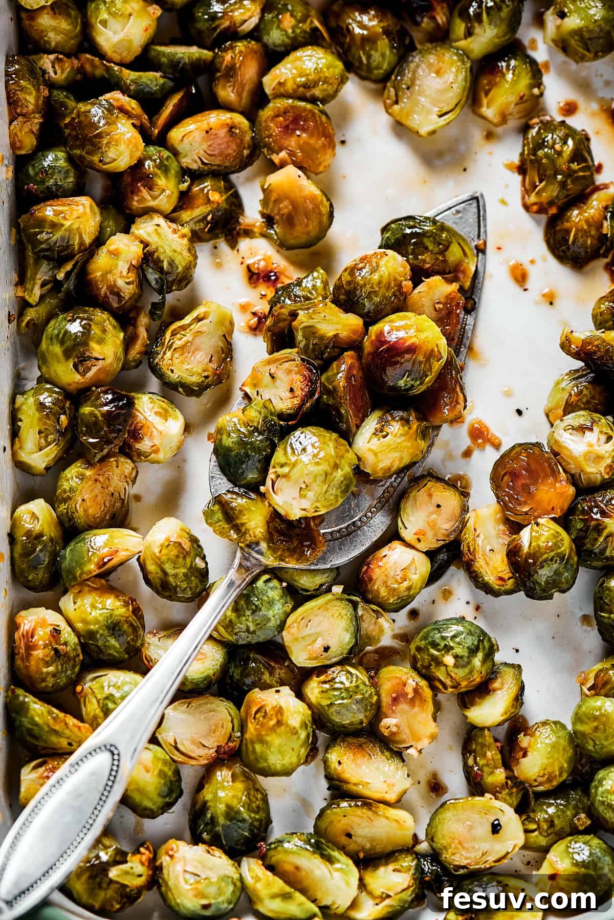 These Roasted Brussels Sprouts are oven-roasted with garlic and drizzled with a killer maple-pomegranate glaze. A veggie side you’ll crave! Tossing roasted Brussels sprouts with the maple-pomegranate glaze on a baking sheet, showcasing their glossy finish.
