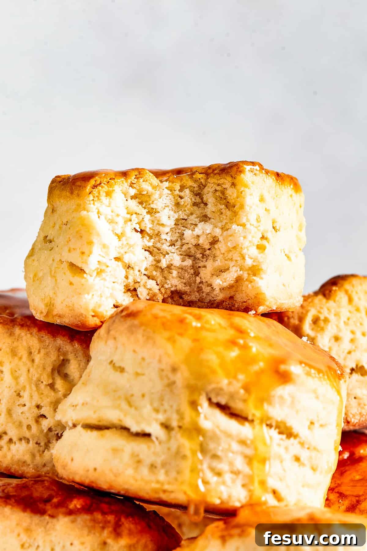 Easy Homemade Biscuits are a buttery, flaky must-have for special meals, and they are so simple to make! Fluffy, melt-in-your-mouth biscuits. A stack of golden-brown, fluffy homemade biscuits piled on an elegant cake plate. One biscuit has a bite taken out, revealing its soft, airy interior. This image perfectly captures the appeal of warm, tender biscuits.