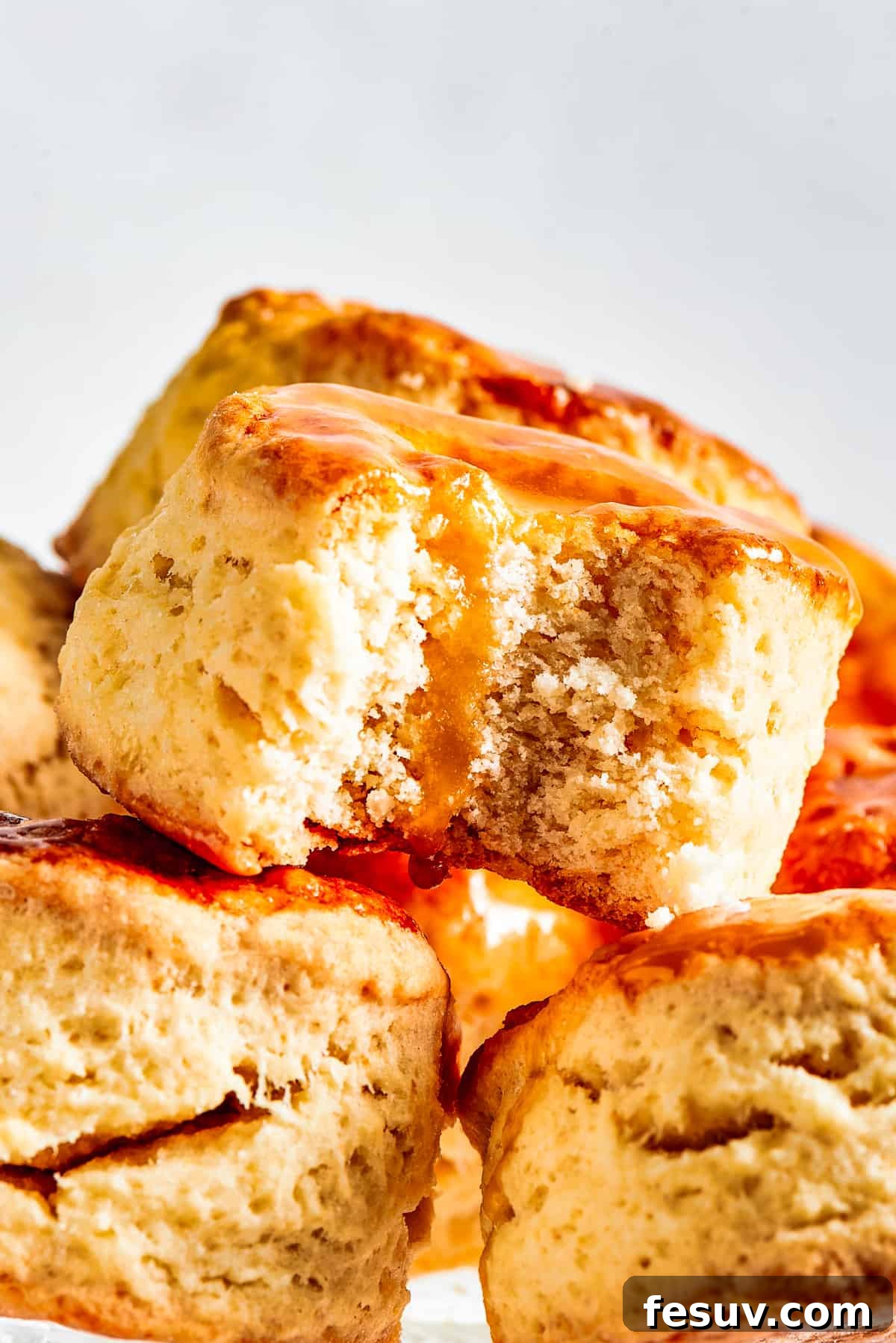 Easy Homemade Biscuits are a buttery, flaky must-have for special meals, and they are so simple to make! Fluffy, melt-in-your-mouth biscuits. A generous pile of homemade biscuits sits on a cake plate, with one biscuit showing a bite taken out, enticing viewers with its flaky texture.