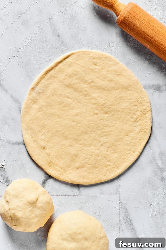 A piece of calzone dough, expertly rolled into a thin, even circle on a floured work surface.