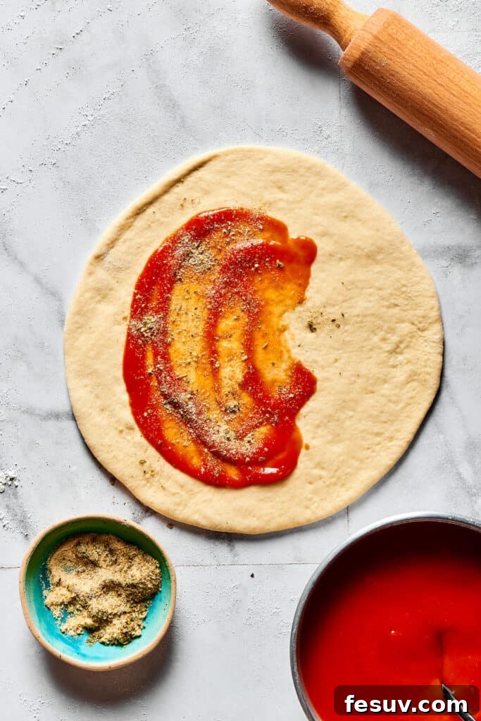 Half of a rolled dough circle generously spread with rich pizza sauce and a sprinkle of seasonings, ready for other fillings.