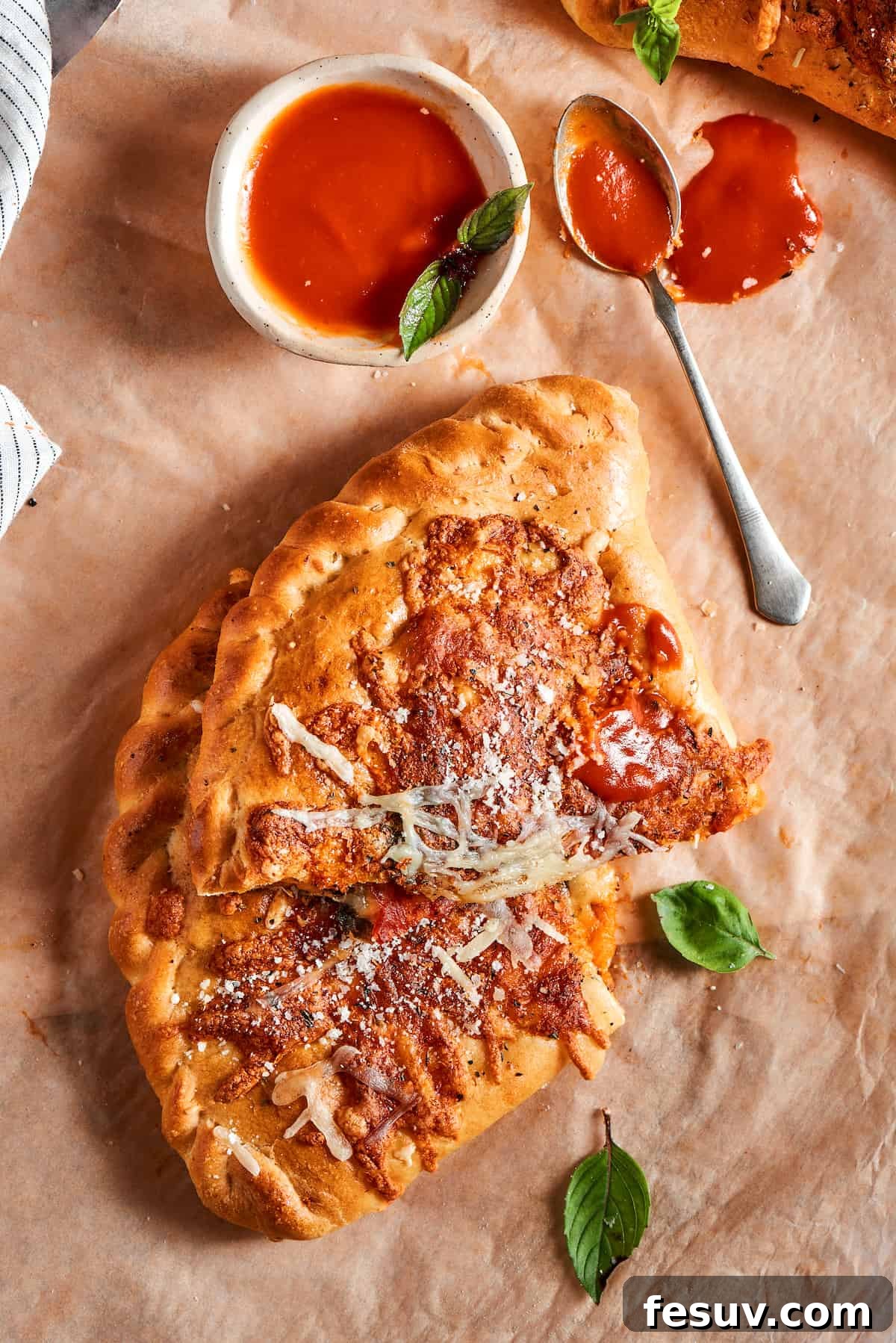 A perfectly baked calzone, sliced in half, sits on a parchment-lined surface next to a small bowl of rich red dipping sauce, inviting a delicious meal.