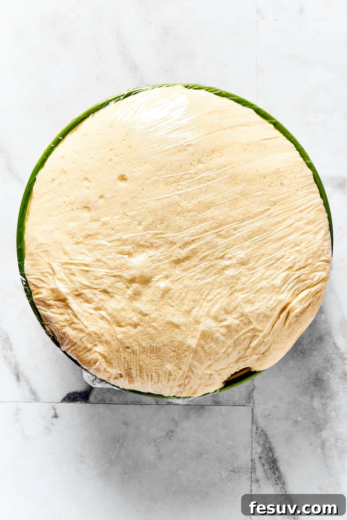 A large mixing bowl containing perfectly risen calzone dough, fluffy and expanded, covered with a dry towel.
