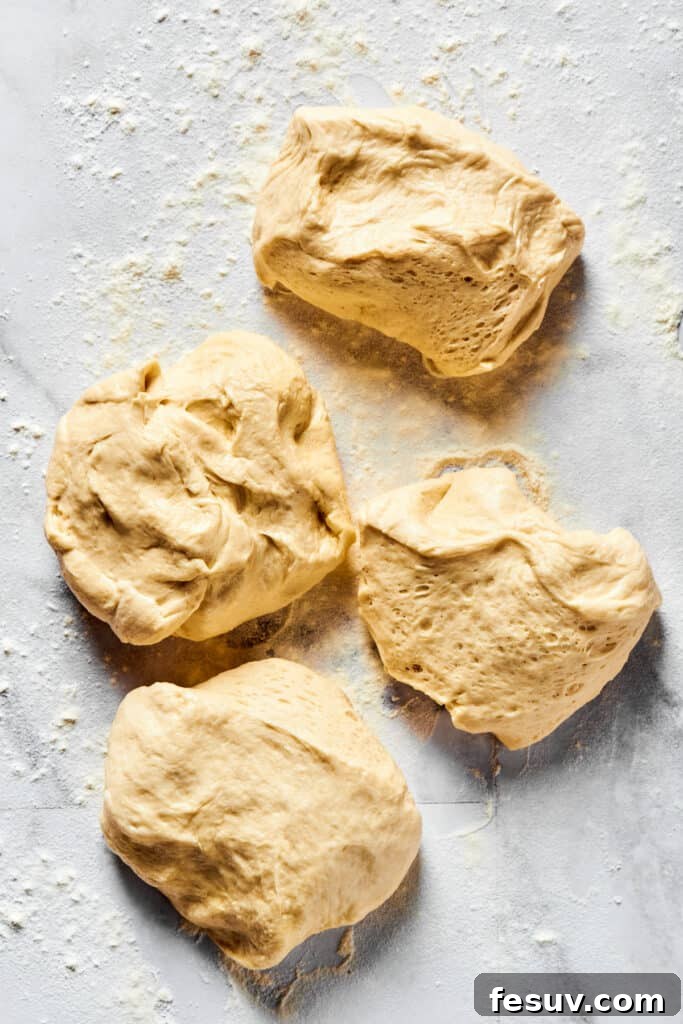 Calzone dough accurately portioned into four equal pieces, ready for rolling on a floured work surface.