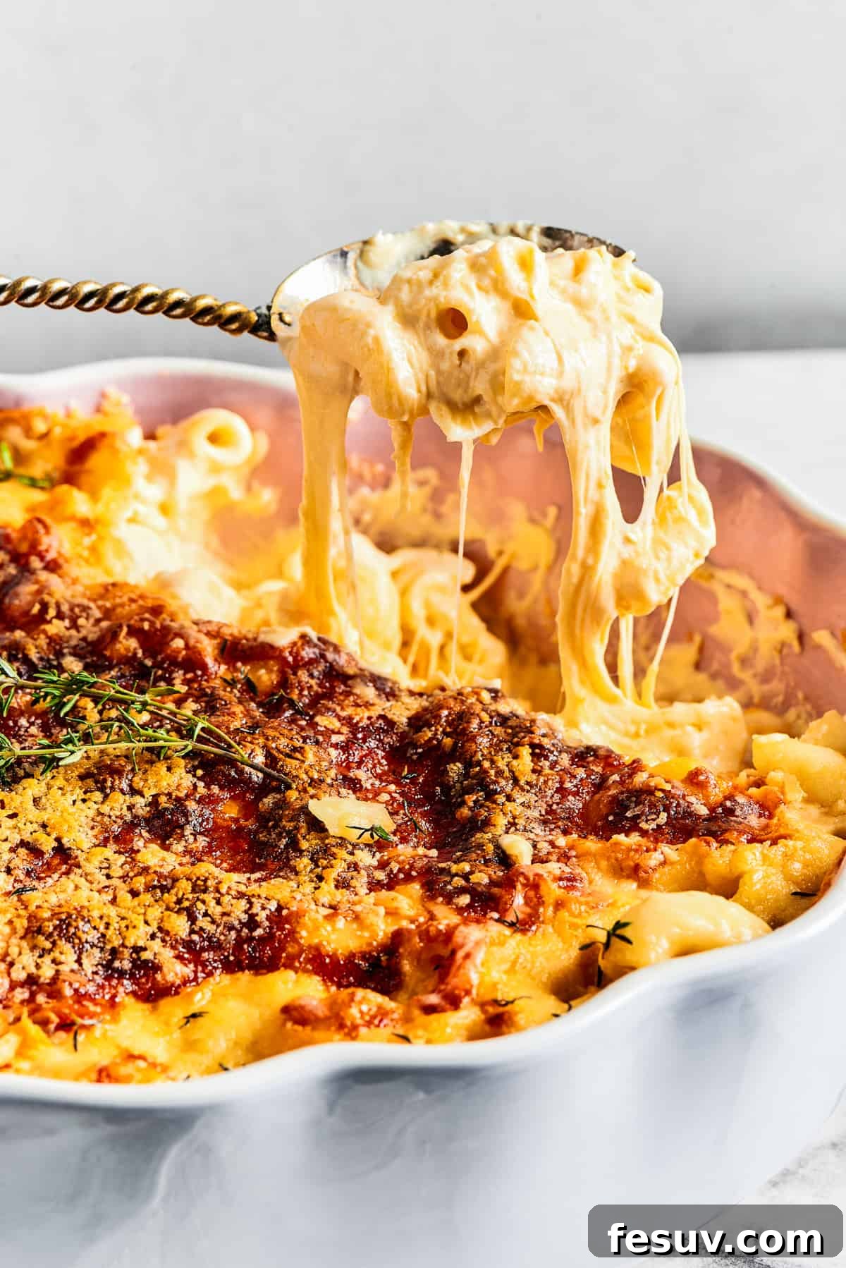 A major family favorite, this ultra-cheesy Baked Macaroni and Cheese is easy to make and perfect for holidays, meatless meals, or anytime! A spoonful of incredibly creamy baked mac and cheese being lifted from a fluted baking dish, demonstrating its rich, gooey texture and delicious pull.