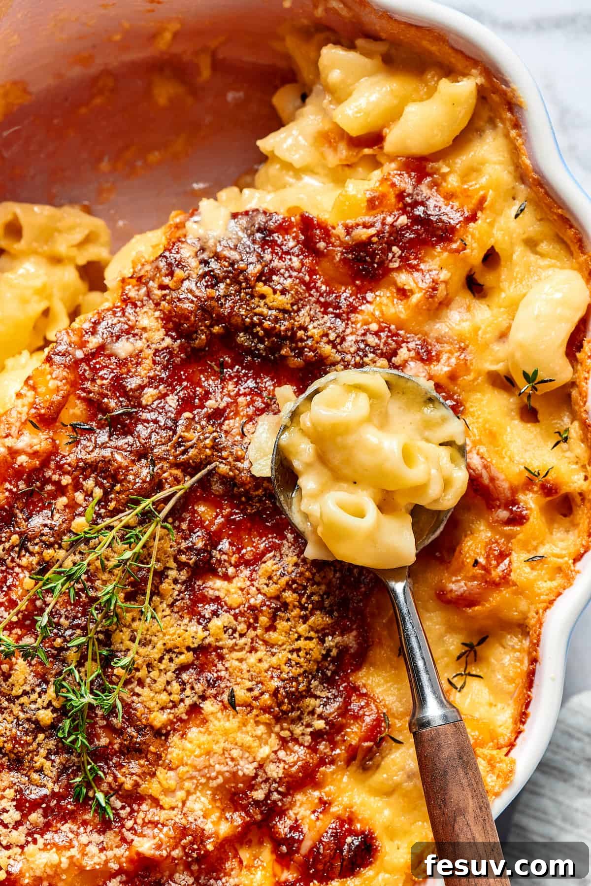A major family favorite, this ultra-cheesy Baked Macaroni and Cheese is easy to make and perfect for holidays, meatless meals, or anytime! A baking dish of golden-brown baked mac and cheese, with a corner scooped out and a serving spoon resting inside, showing the creamy interior and crispy top.
