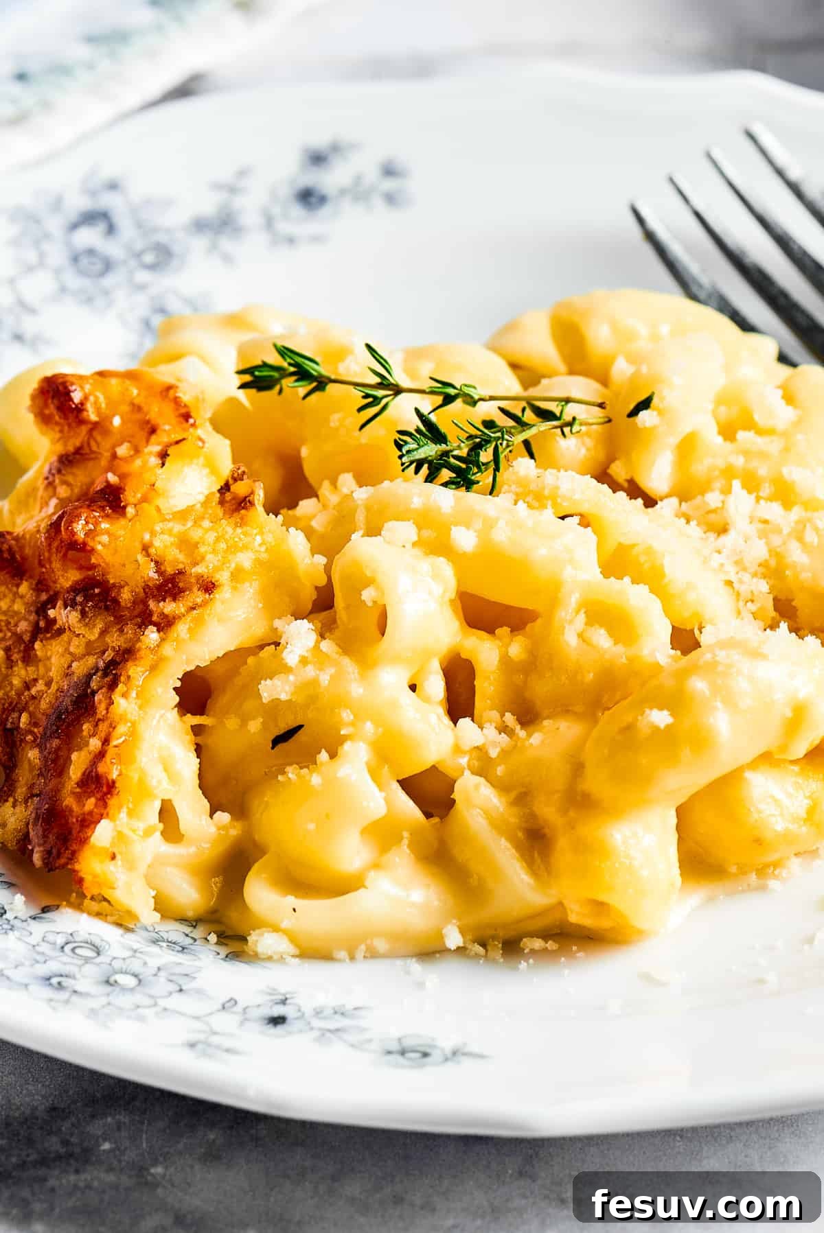 A major family favorite, this ultra-cheesy Baked Macaroni and Cheese is easy to make and perfect for holidays, meatless meals, or anytime! A decorative plate holding a generous serving of baked macaroni and cheese, garnished with fresh herbs, showcasing its appetizing appeal.
