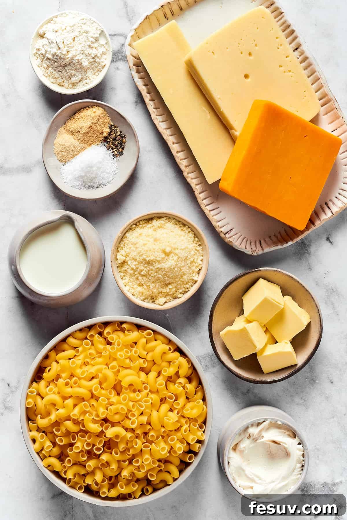 A major family favorite, this ultra-cheesy Baked Macaroni and Cheese is easy to make and perfect for holidays, meatless meals, or anytime! A vibrant flat lay arrangement of all the essential ingredients for baked mac and cheese, including elbow pasta, various cheeses like gouda, mozzarella, and cheddar, fresh thyme, butter, flour, milk, heavy cream, and a selection of seasonings.