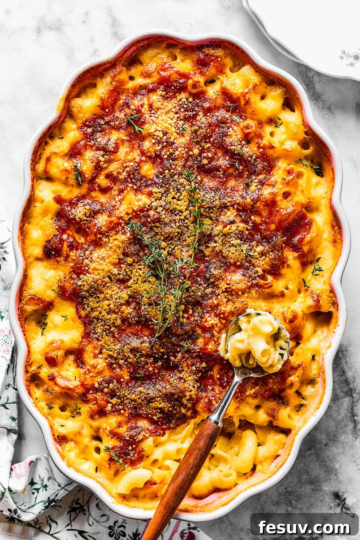 A major family favorite, this ultra-cheesy Baked Macaroni and Cheese is easy to make and perfect for holidays, meatless meals, or anytime! A serving spoon scoops a generous portion of baked macaroni and cheese from a casserole dish, showcasing its rich, golden-brown top and creamy interior.