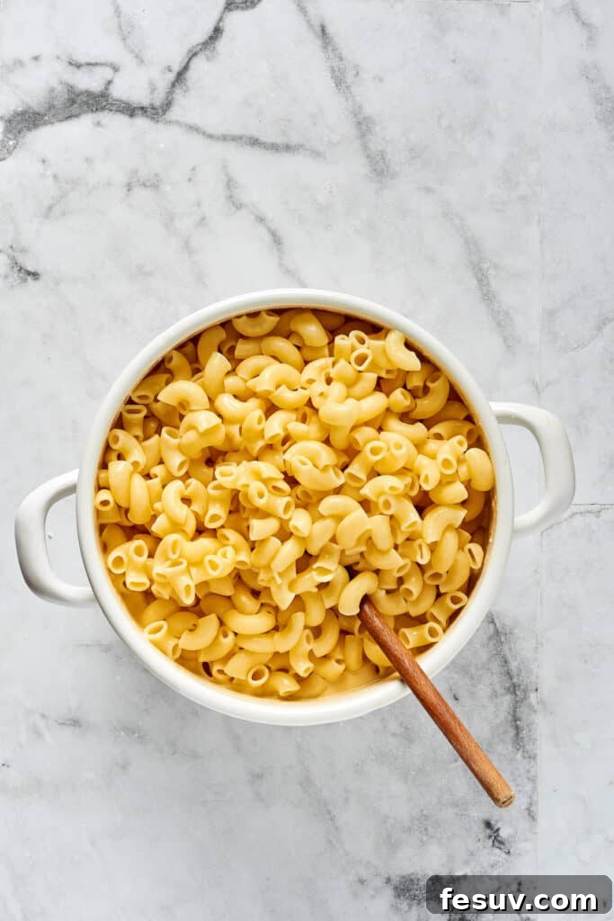Golden Crusted Macaroni Delight 6 Cooked elbow pasta being stirred into a rich, creamy cheese sauce in a large pot, ensuring every noodle is coated.