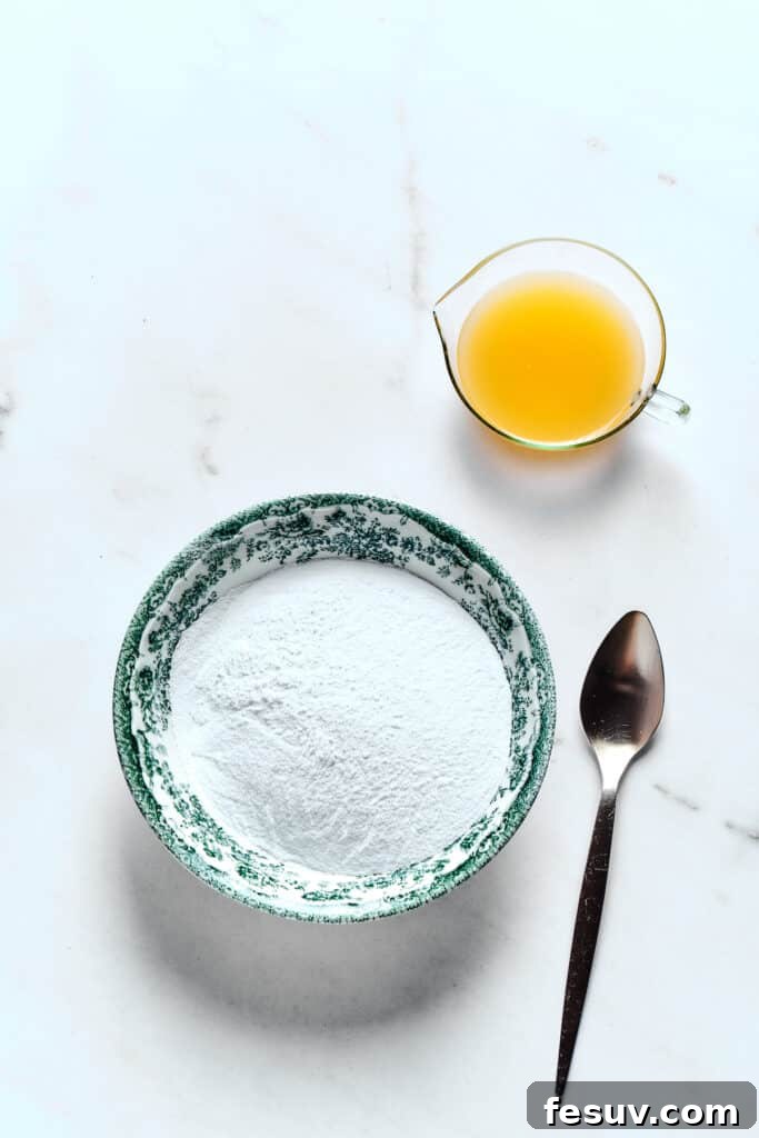 Winterberry Pound Cake Bliss 12 A bowl of finely sifted powdered sugar sits beside a glass of freshly squeezed orange juice, with a spoon nearby, ready for glaze preparation.