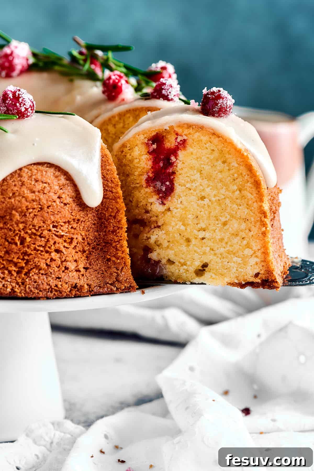 Winterberry Pound Cake Bliss 16 A hand gently lifts a perfect slice of cranberry pound cake from a cake stand using a silver cake server, showcasing its delicious layers and cranberries.