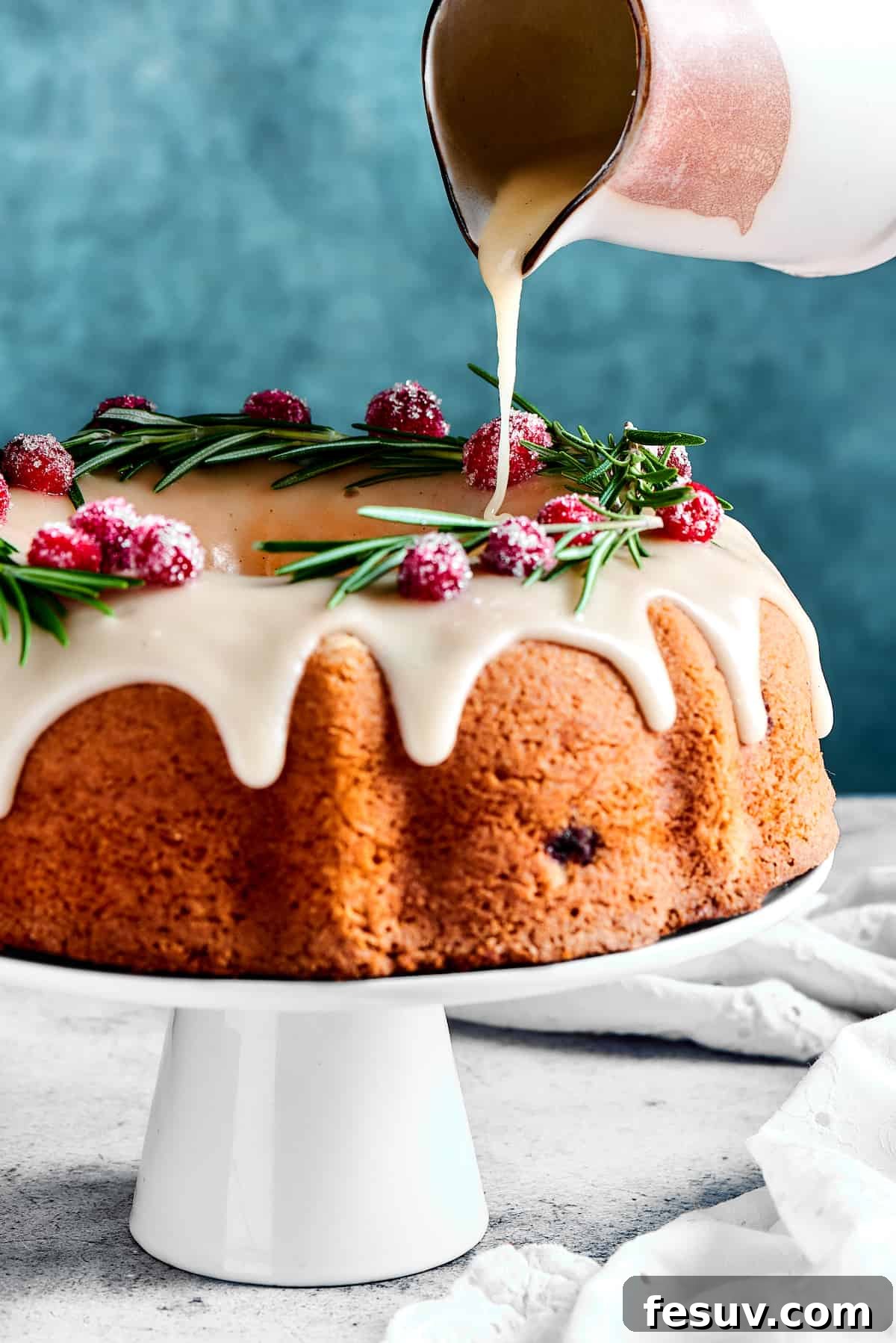 Winterberry Pound Cake Bliss 5 Someone pouring a thick, glossy orange glaze over a freshly baked Bundt cake, allowing it to drip down the sides.