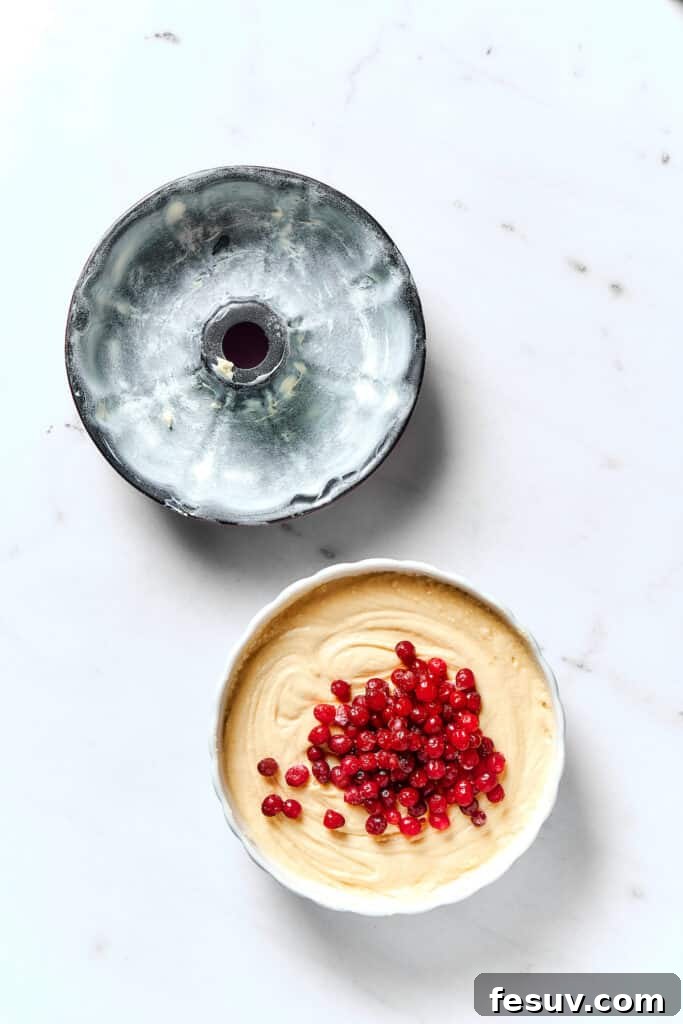 Winterberry Pound Cake Bliss 10 A perfectly buttered and floured Bundt pan sits next to a mixing bowl brimming with rich cake batter, sprinkled with fresh cranberries.