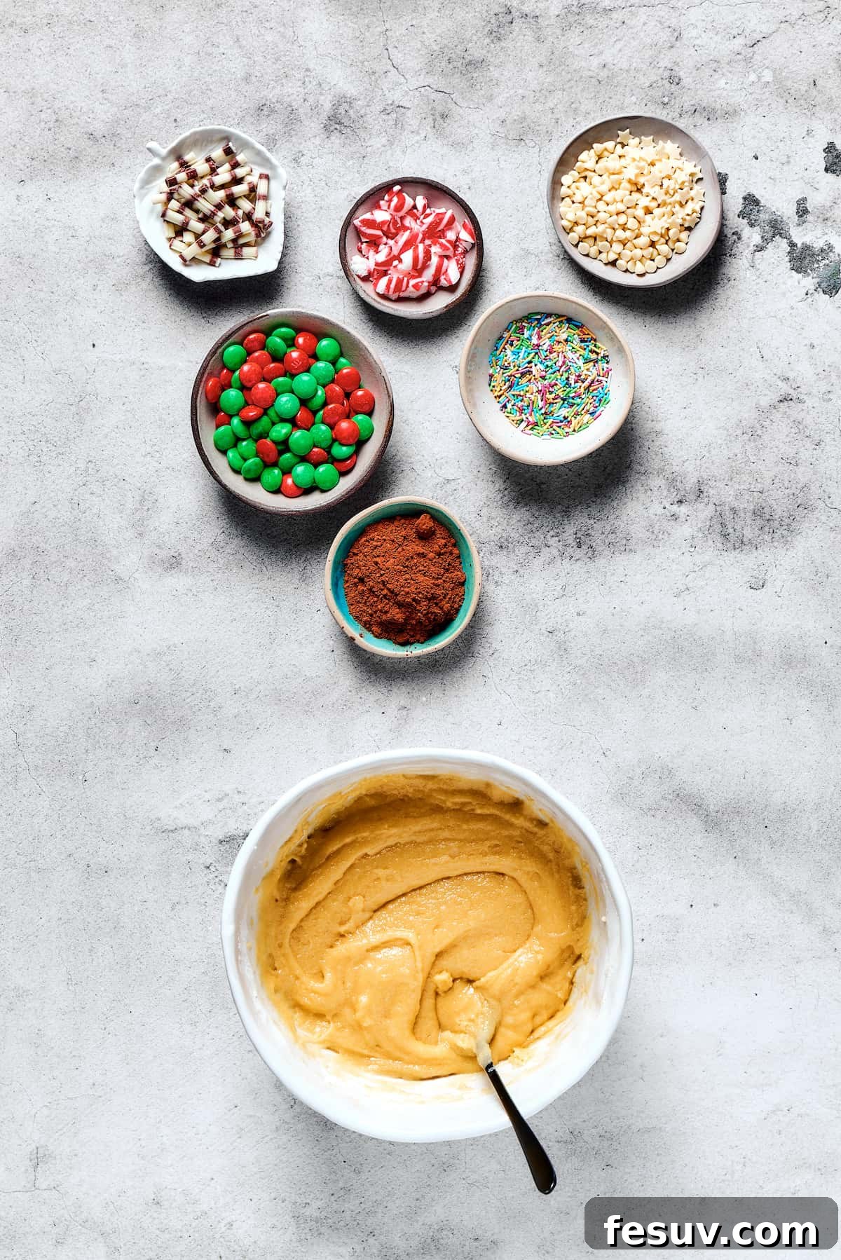 A bowl of freshly mixed, creamy cookie dough rests beside small, inviting dishes filled with an assortment of vibrant decorations.