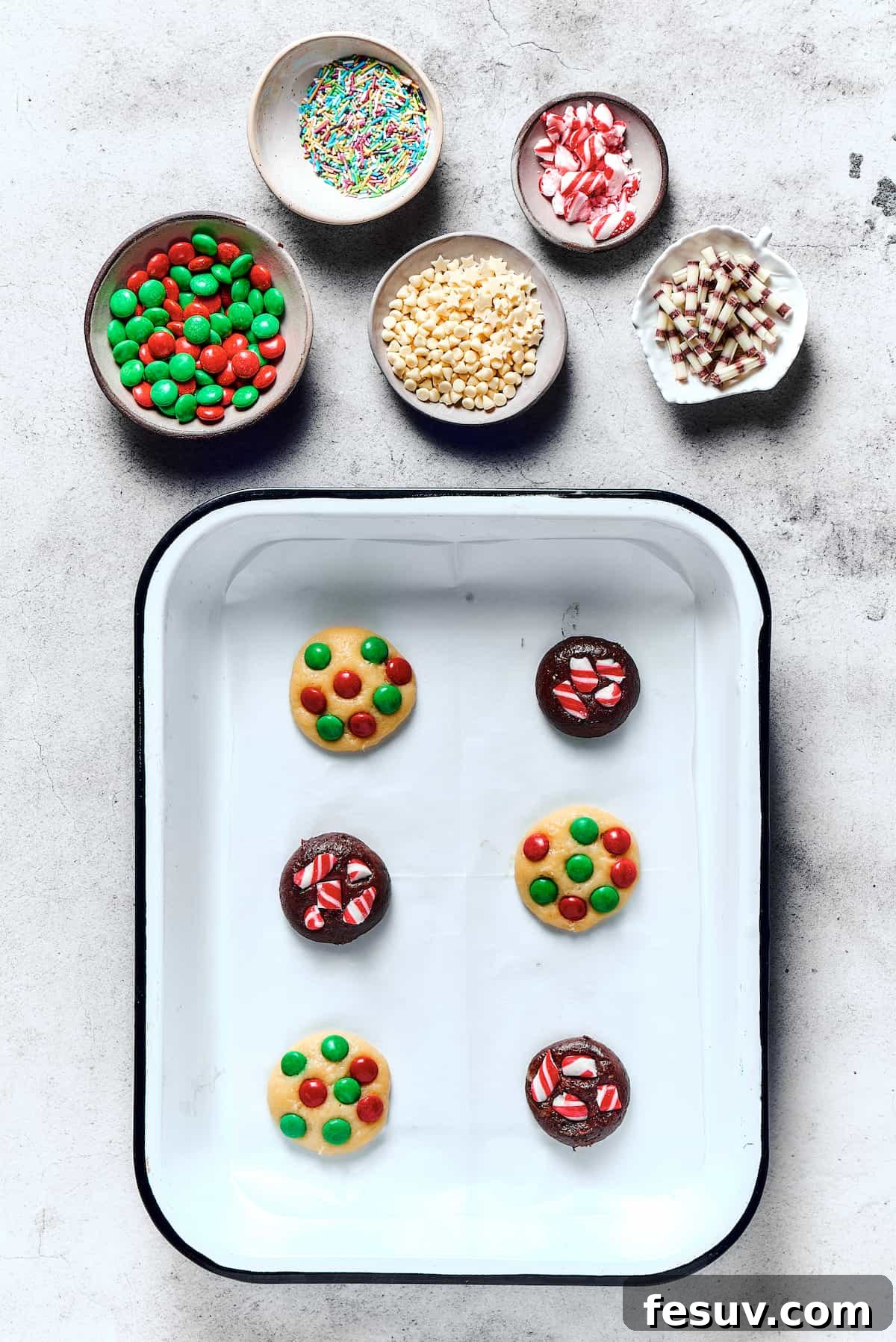 A baking sheet laden with unbaked chocolate and vanilla cookies, each featuring vibrant M&M's pressed into the soft dough, ready for the oven.