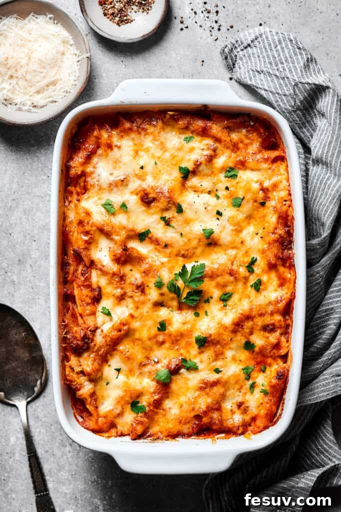 Baked Mostaccioli is a wholesome pasta dinner prepared with a homemade tomato sauce including Italian sausage, ground beef, and lots of cheese! Freshly baked mostaccioli casserole, golden and bubbly, garnished with vibrant fresh herbs, presented in a baking dish.