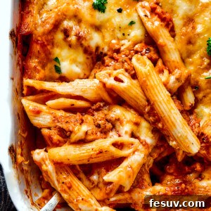 Scooping out a spoonful of baked mostaccioli from a large baking dish.