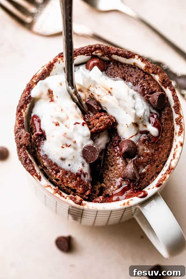 This moist and indulgent Chocolate Mug Cake cooks in one minute inside the microwave. It is the most perfect, individual-sized dessert! A spoon digging into a rich, moist chocolate cake inside a mug, highlighting its indulgent texture.