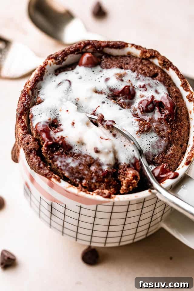 This moist and indulgent Chocolate Mug Cake cooks in one minute inside the microwave. It is the most perfect, individual-sized dessert! A spoon scooping a bite of chocolate mug cake topped with a dollop of whipped cream, showing its moist interior.