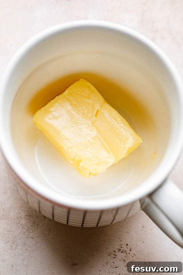 This moist and indulgent Chocolate Mug Cake cooks in one minute inside the microwave. It is the most perfect, individual-sized dessert! Two tablespoons of butter melting in a microwave-safe mug, ready for the next steps of the chocolate mug cake recipe.