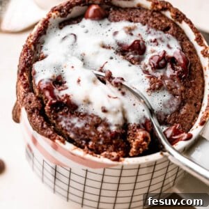 A spoon scooping a bite of chocolate mug cake topped with a dollop of whipped cream, showing its moist interior.