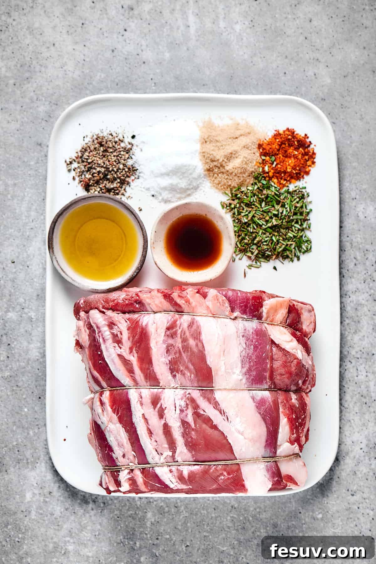 Making the perfect Prime Rib is easy! A few flavorful herbs and spices plus an easy reverse-sear roasting method are all you need. Seasonings, oil, worcestershire sauce, and a tied prime rib roast on an enamel tray.