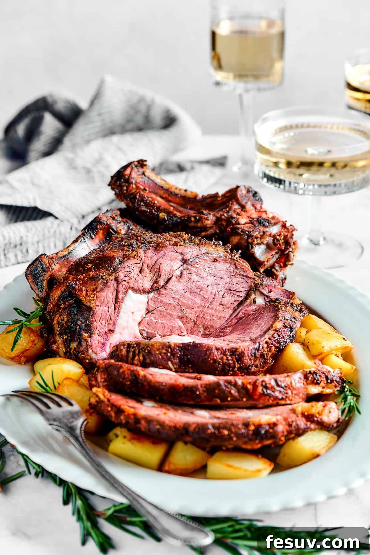 Making the perfect Prime Rib is easy! A few flavorful herbs and spices plus an easy reverse-sear roasting method are all you need. A bone-in rib roast, cooked and plated on a white serving dish.