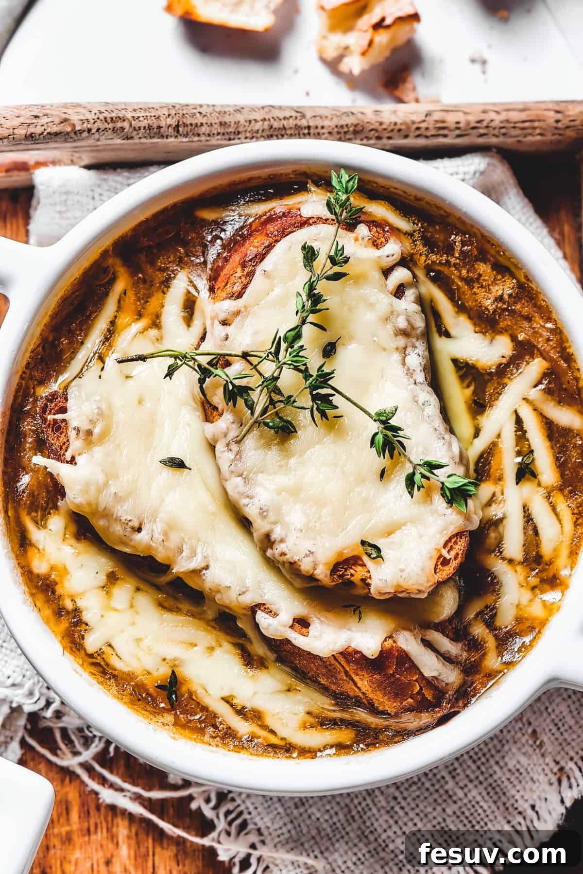 Savor the ultimate French Onion Soup: Rich, caramelized onion broth, topped with a crusty baguette and perfectly melted Gruyère and Swiss cheese. Overhead shot of French Onion Soup bowls, garnished with fresh thyme sprigs and golden-brown cheesy croutons.