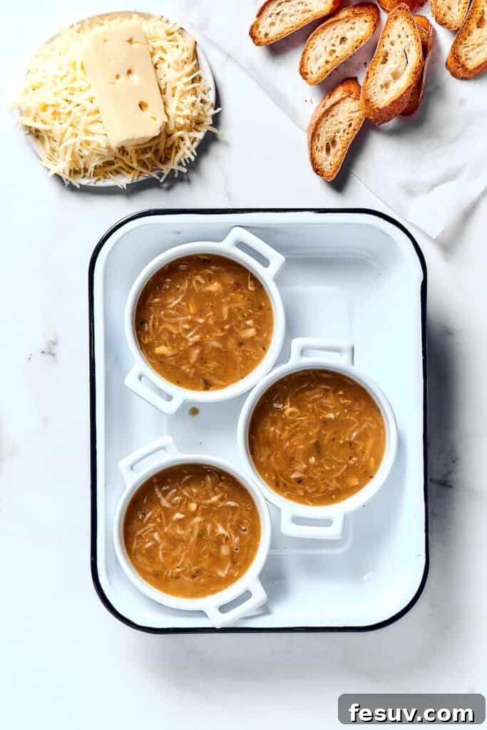 Caramelized Onion Elixir 8 Individual oven-proof bowls of French onion soup waiting next to toasted baguette slices and a dish of shredded Gruyère and Swiss cheese.