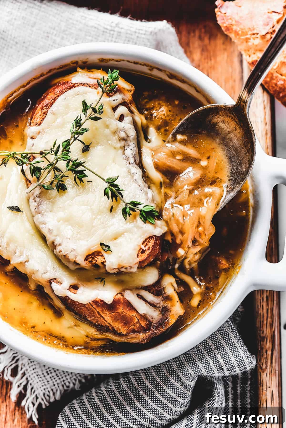 Enjoy a spoonful of hearty French Onion Soup, a perfect blend of rich broth, sweet onions, and melted cheese. A spoon scooping a generous portion of French onion soup from a bowl, highlighting the rich broth and caramelized onions.