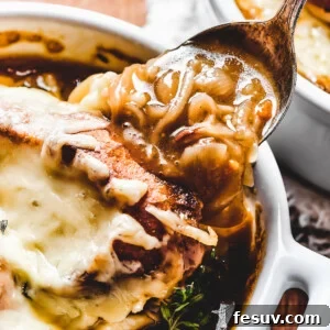 A spoon scooping a generous portion of French onion soup from a bowl, highlighting the rich broth and caramelized onions.