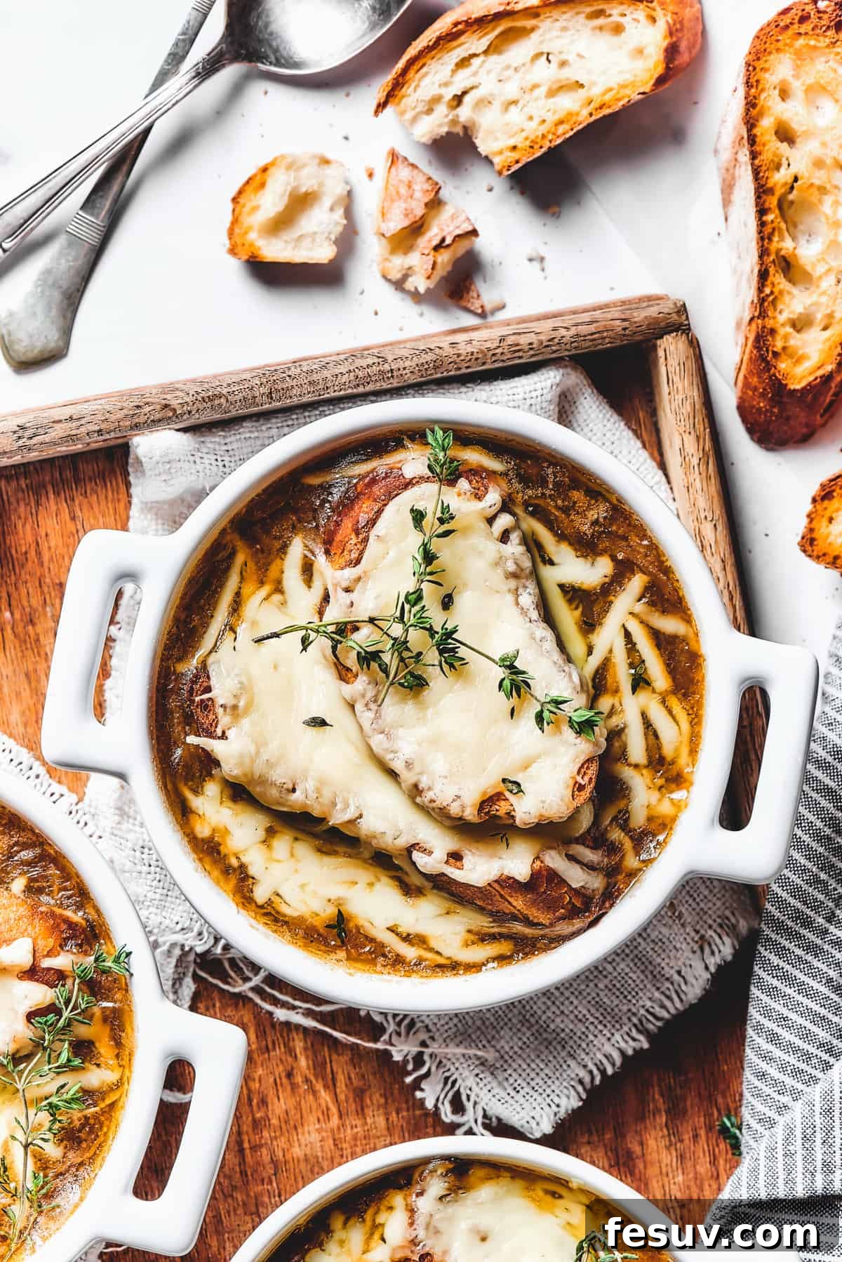 Experience the warmth of classic French Onion Soup, a rich and comforting dish topped with cheesy baguette. Elegant double-handled bowls filled with steaming French onion soup, topped with golden-brown cheesy croutons, presented on a wooden tray.