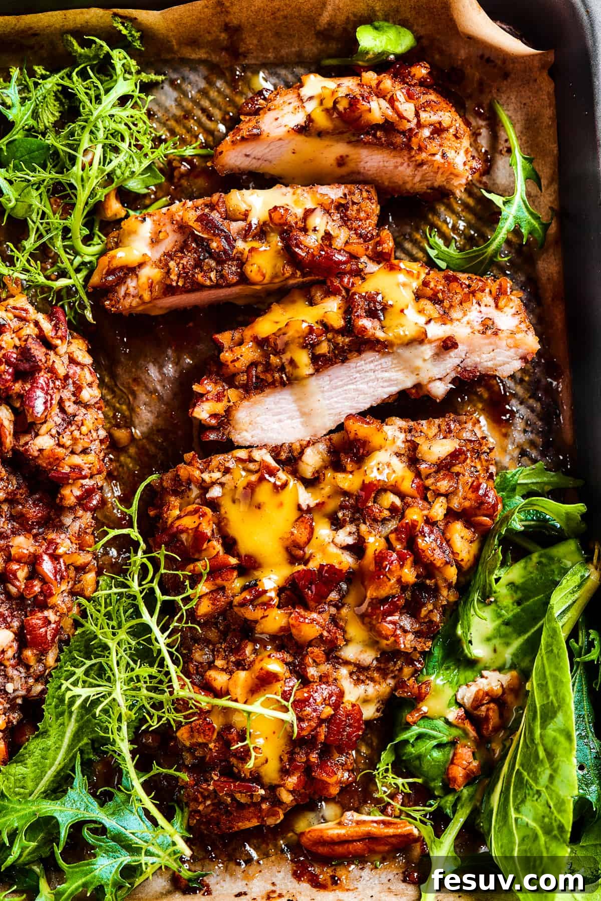 Sliced pecan chicken on a serving dish, with greens placed around the chicken.
