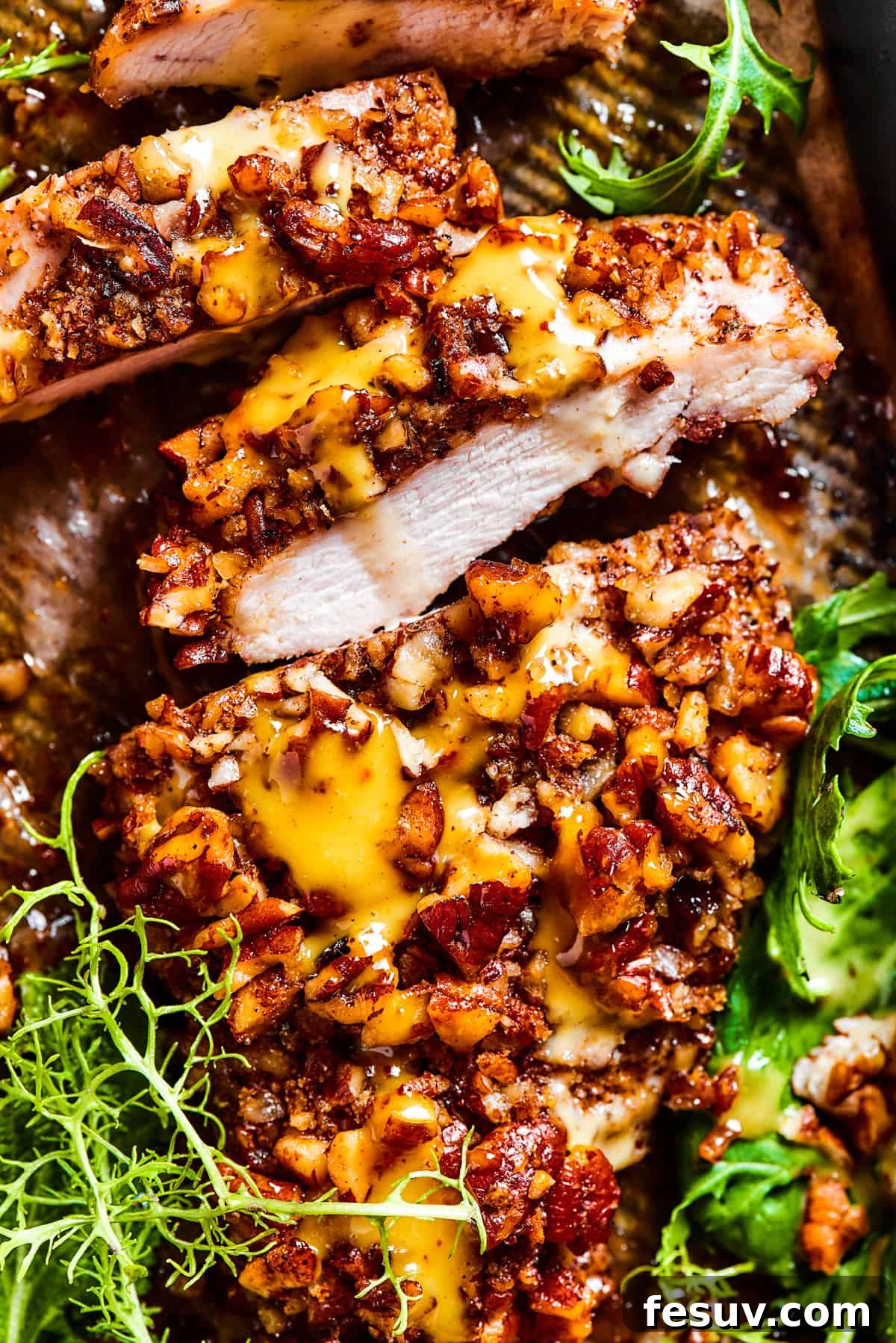 Sliced pecan chicken on a serving dish, with greens placed around the chicken.