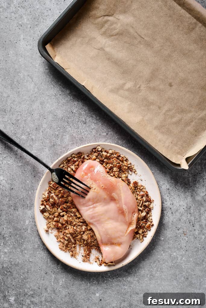 Raw chicken being coated in a ground pecan mixture.