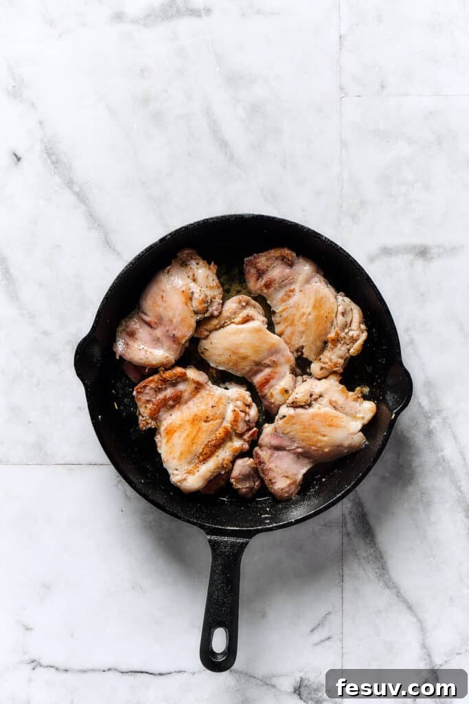 Velvety Chicken Gnocchi Delight 2 Chicken thighs browning in a skillet, seasoned with herbs.