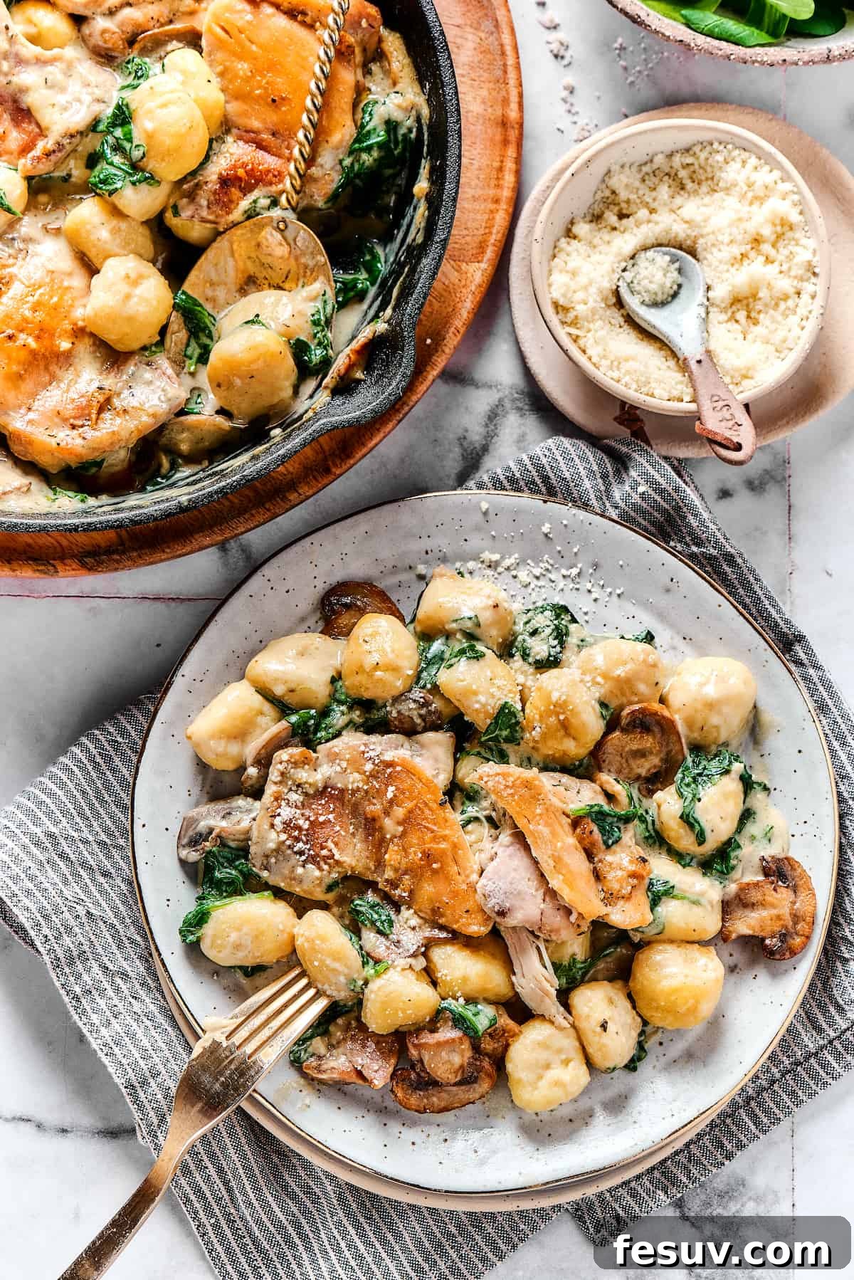 Creamy Chicken & Gnocchi is a bold, yet comforting combo of tender chicken, pillowy gnocchi, and flavorful spinach and mushrooms. Overhead shot of a chicken skillet dish served onto a dinner plate, garnished with fresh herbs.