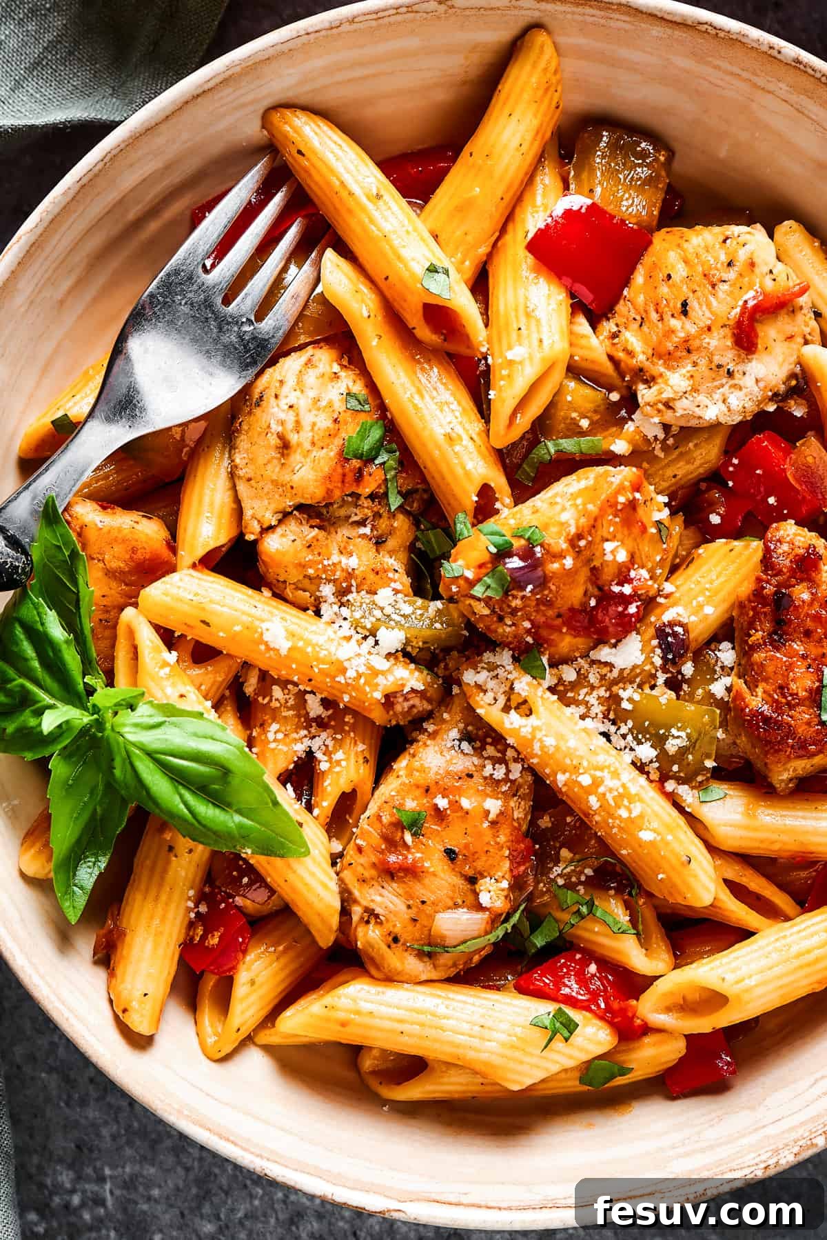Overhead close-up shot of colorful Chicken Fajita Pasta, featuring penne, chicken, vibrant peppers, and tomatoes, garnished with fresh herbs.