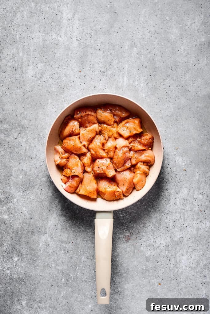 Raw, seasoned chicken pieces sizzling in a hot skillet, beginning to brown.