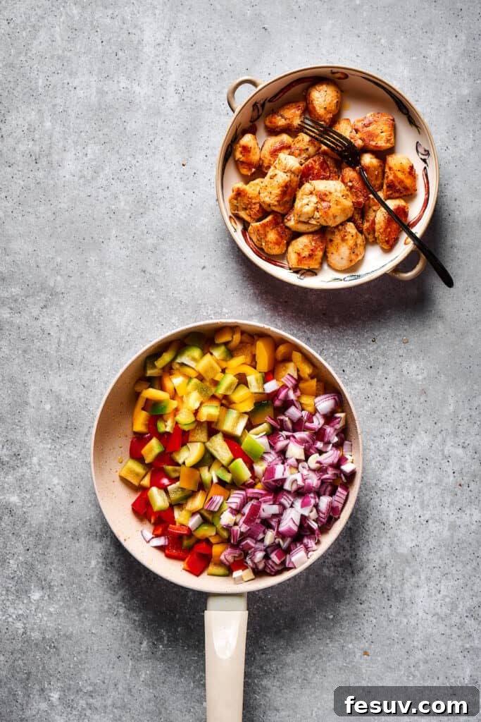 Finely chopped onions and colorful bell peppers sautéing in a skillet, next to a bowl of perfectly cooked chicken.