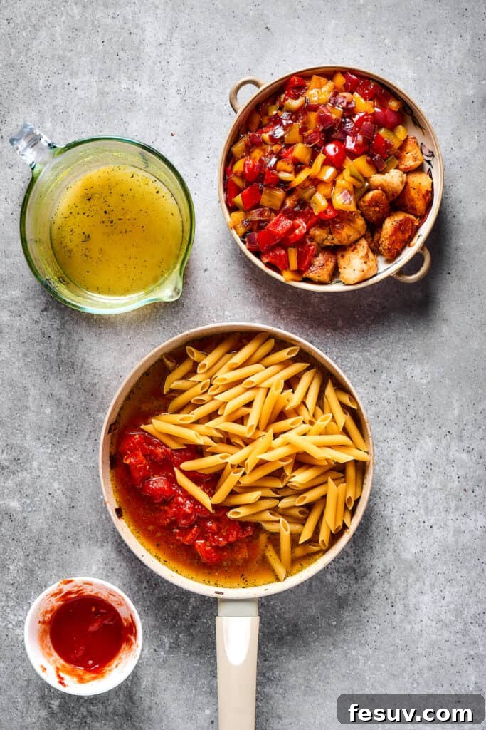 Penne pasta, crushed tomatoes, and chicken broth simmering in a skillet, positioned alongside a plate of cooked chicken and sautéed vegetables.