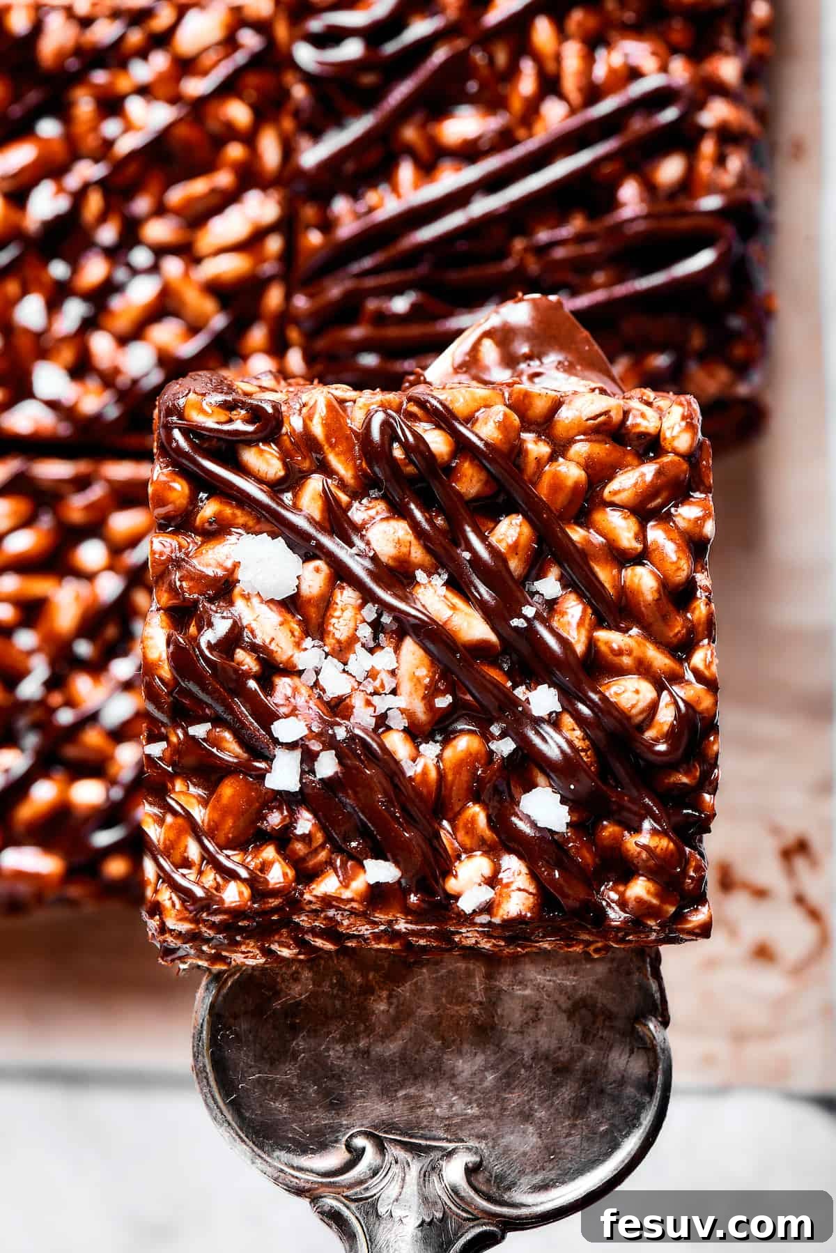 Chocolate Rice Krispie Treats are light and crunchy, with a sticky marshmallow texture and real dark chocolate. Easy and scrumptious! Lifting a chocolate cereal bar square with a silver dessert server.
