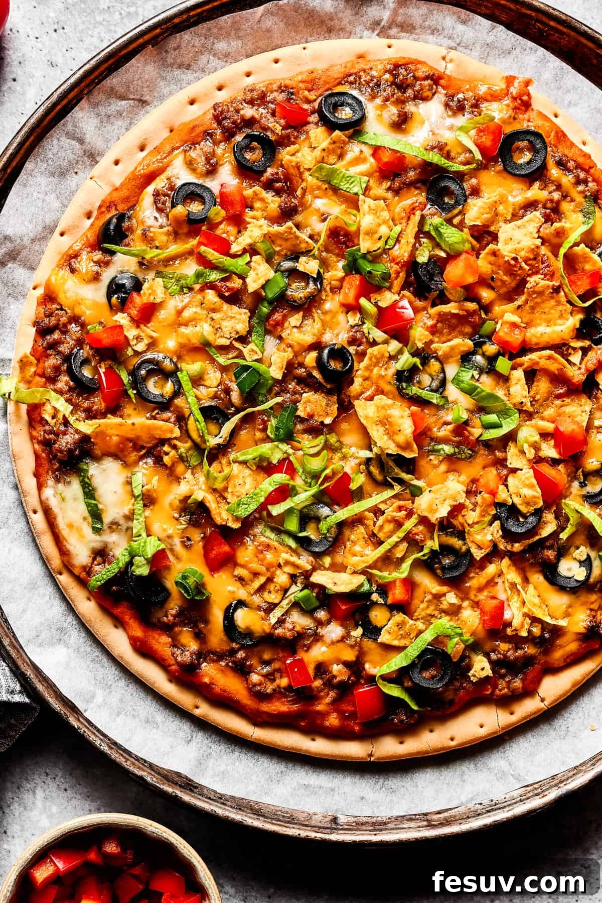 A freshly baked taco pizza, generously adorned with vibrant, fresh toppings like diced tomatoes, shredded lettuce, and green onions.