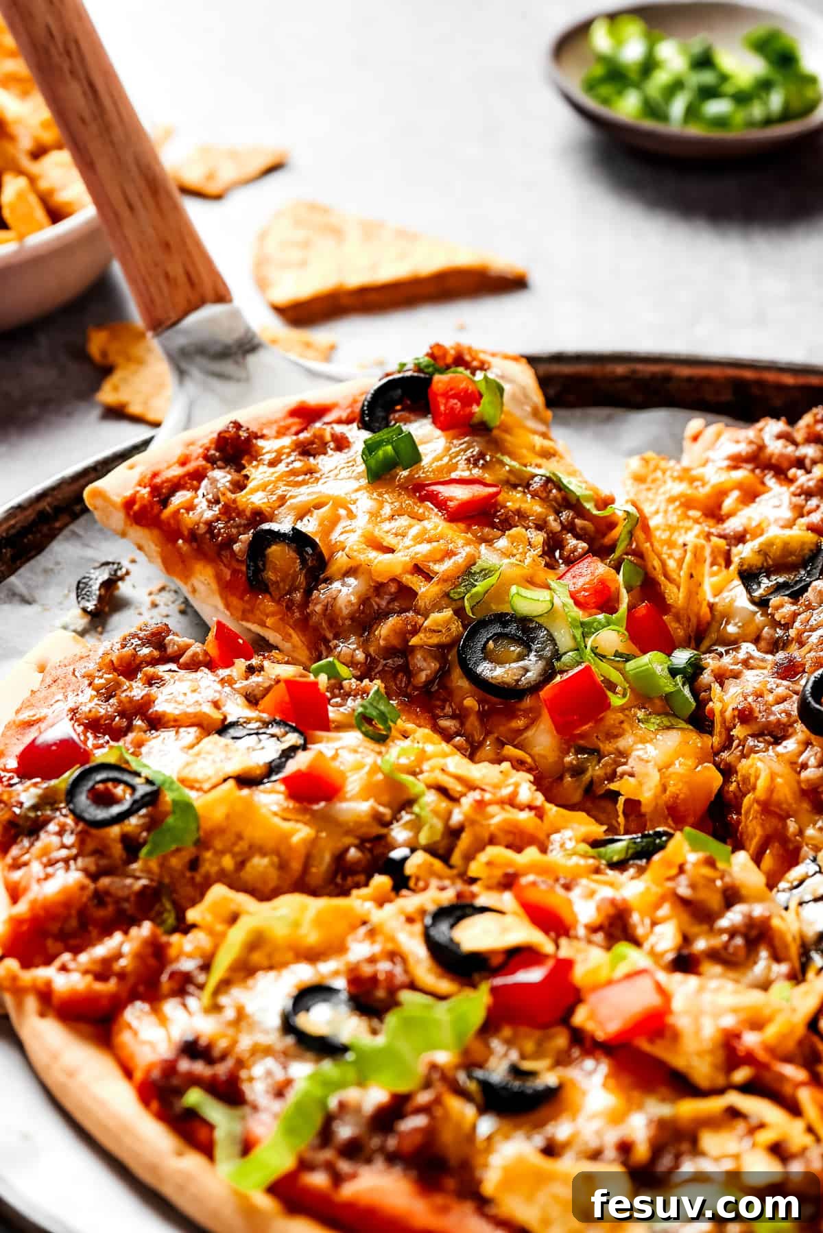 A hand lifting a perfect slice of freshly baked taco pizza with a pie server, showcasing its delicious layers and crisp crust.