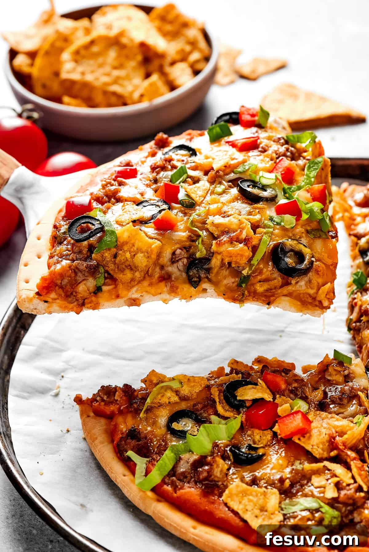 A beautifully sliced taco pizza on a wooden cutting board, with a pie server lifting one slice, and another slice waiting on a small plate in the background.