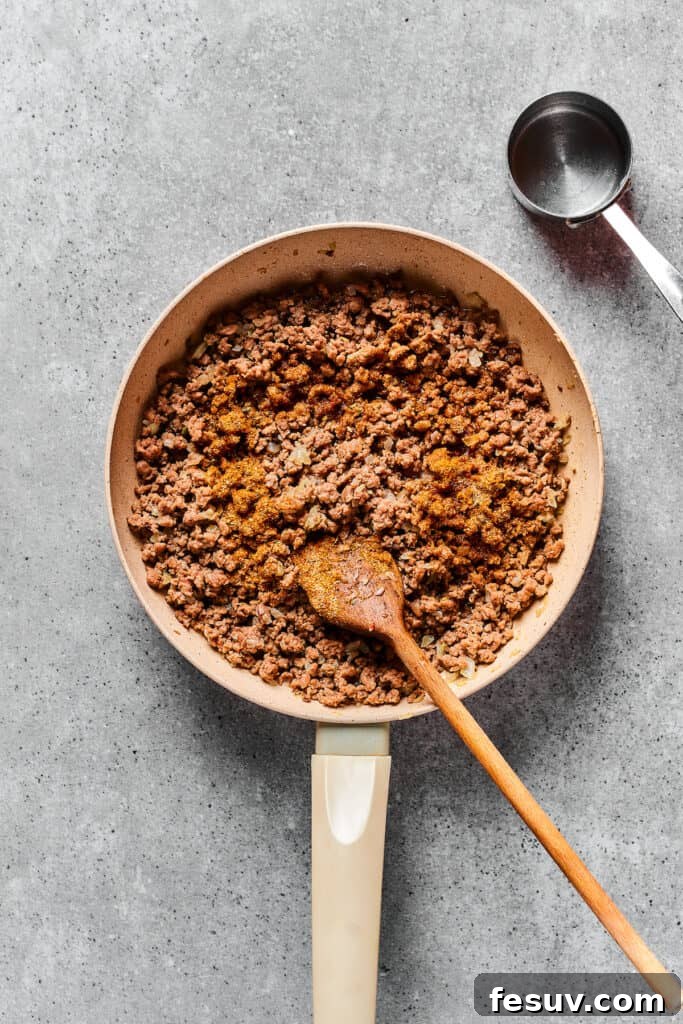 Perfectly cooked and seasoned taco meat in a skillet, ready for pizza assembly.