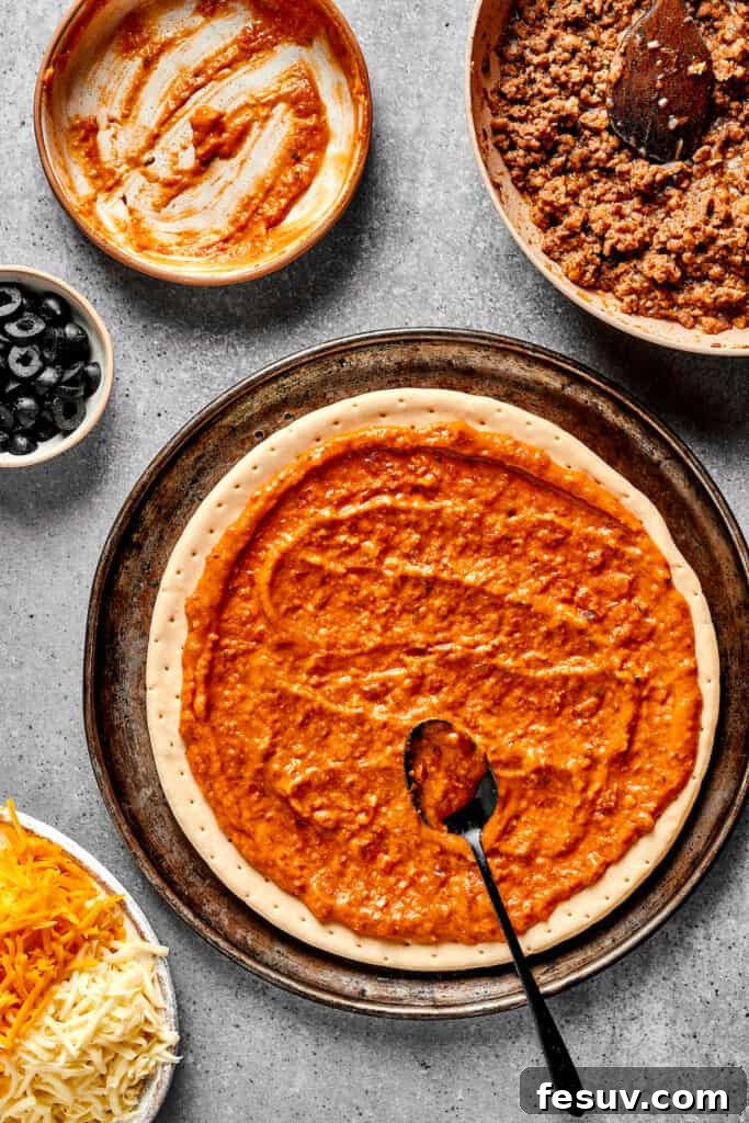 Spreading a rich refried bean and salsa mixture evenly over a prepared pizza crust.